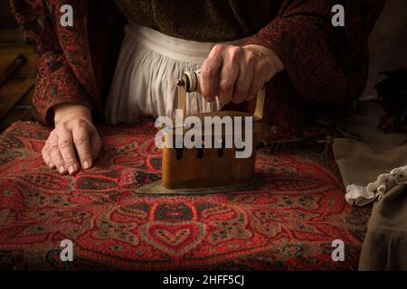 Vecchia donna in abito vittoriano che lavora con un ferro di carbone antico su un asse Foto Stock