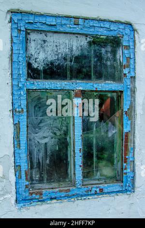 Vista della vecchia casa abbandonata finestra con vetro rotto e vernice blu pelata. Foto Stock