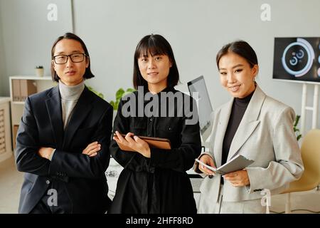 Ritratto della vista frontale del giovane team aziendale asiatico che guarda la fotocamera mentre si trova in ufficio Foto Stock