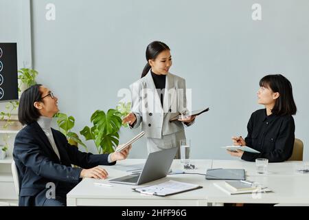 Il gruppo di uomini d'affari asiatici che si riuniscono in ufficio si concentra sulla giovane donna che istruisce i colleghi Foto Stock