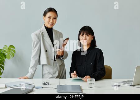 Ritratto minimo di due giovani donne d'affari asiatiche sorridenti alla macchina fotografica in ufficio godendo di lavoro, spazio copia Foto Stock