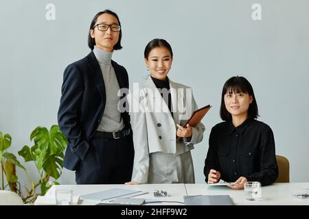 Ritratto minimale del team di affari asiatici sorridente alla macchina fotografica in ufficio godendo il lavoro Foto Stock