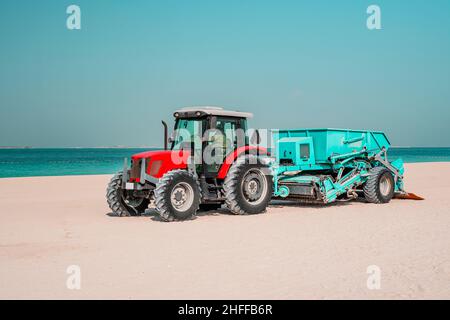 Trattore rosso sulla spiaggia sabbiosa pulizia, escavatore lavoro sulle dune di sabbia, trattore levigatura la sabbia su spiaggia pubblica Foto Stock