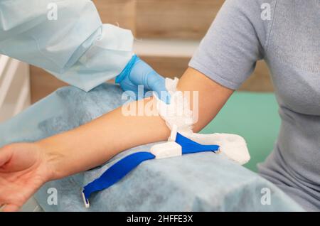 Il medico mette un bendaggio sul braccio del donatore. Applicazione di un bendaggio adesivo su una mano femminile di cotone dopo aver prelevato il campione di sangue dalla vena Foto Stock