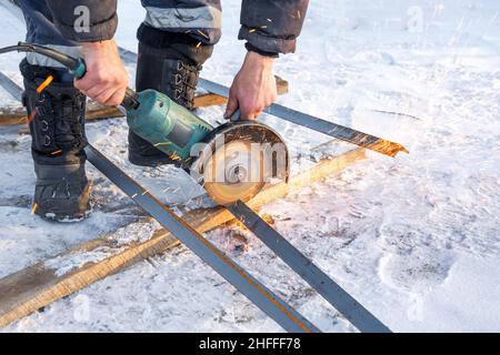 Taglio di un'asta di metallo con una sega circolare in inverno primo piano foto di un uomo che tiene una sega circolare e taglia un'asta di metallo. Le scintille volano Foto Stock