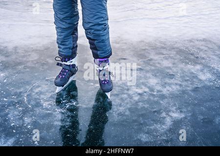 Vista sul bel ghiaccio blu trasparente del lago Baikal ghiacciato. L'uomo nei pattini viaggia sul ghiaccio. Attività invernali all'aperto. Foto Stock