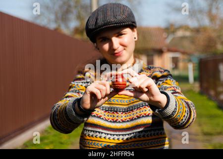 Felice sorridente donna che tiene un uovo rosso colorato, Pasqua concetto di vacanza. Mani che tengono moderne uova di pasqua dipinte. Giovane hipster donna millennial in Foto Stock