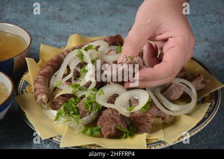 Beshbarmak - piatto nazionale kazako, preparato con carne e pasta. Piatto di Beshbarmak primo piano su un piatto sul tavolo. Grandi pezzi di carne stufata e oni Foto Stock