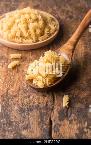 varietà di pasta cruda in un cucchiaio di legno, su sfondo di legno, dieta e concetto di cibo, preso in profondità di campo poco profonda con spazio copia Foto Stock