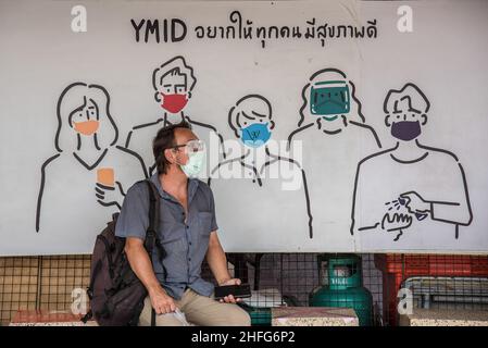 Bangkok, Tailandia. 16th Jan 2022. Un uomo che indossa maschera facciale come misura preventiva contro la diffusione del convivid-19 si siede vicino a una bandiera pubblicitaria al Monumento della Vittoria a Bangkok. (Foto di Peerapon Boonyakiat/SOPA Images/Sipa USA) Credit: Sipa USA/Alamy Live News Foto Stock