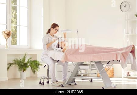 Il medico estetista sta esaminando il viso della donna con una lampada  speciale Foto stock - Alamy