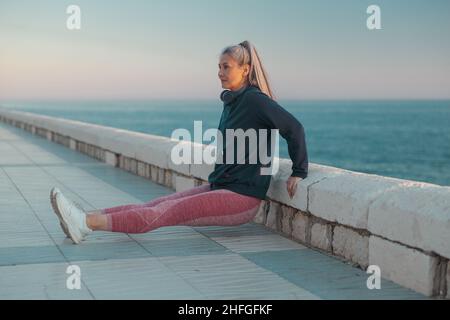 Sportswoman asiatico con cappuccio nero che fa reverse push-up vicino al mare Foto Stock