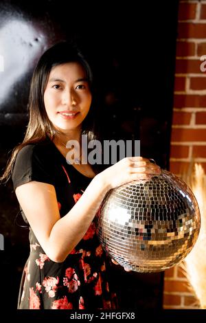 Giovane donna dell'Asia orientale in stampa floreale vestito che tiene una sfera dello specchio Foto Stock