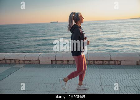 Sportivo maturo che indossa cuffie e abbigliamento sportivo da jogging sul terrapieno Foto Stock