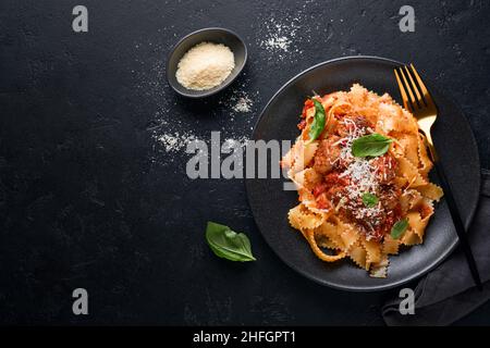 Tagliatelle con polpette di pomodoro, basilico e parmigiano su fondo di pietra nera o cemento. Piatti italiani e cucina tradizionale Foto Stock