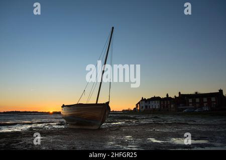 Bosham, porto di Bosham, con barca di legno che poggia sullo scafo accanto alle case del villaggio, tramonto, crepuscolo, marea out, Sussex, Regno Unito, gennaio. Foto Stock