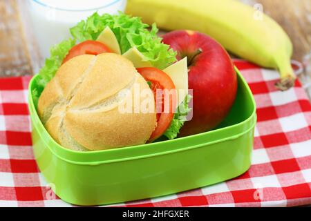 Scatola per il pranzo della scuola con rotolo di formaggio, lattuga e pomodoro, mela e banana Foto Stock