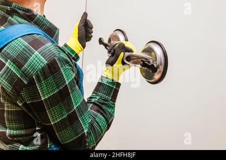 Glazier che tiene nelle mani un pezzo di vetro spesso con l'aiuto di una speciale ventosa, sfondo chiaro Foto Stock