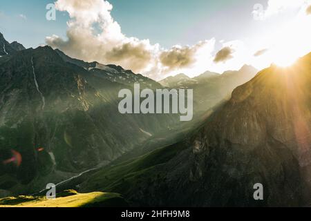 Bel paesaggio di montagna in una serata estiva, i raggi del sole illuminano la valle verde di montagna e le pendici rocciose prima del tramonto Foto Stock