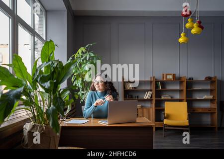 Felice freelancer femmina in spazio di coworking guardare in finestra dopo il successo della videoconferenza riunione Foto Stock
