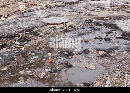 Una strada danneggiata da pioggia e neve, che necessita di manutenzione. Pavimentazione asfaltata rotta con conseguente buche, pericolosa per i veicoli. Foto Stock