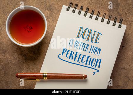 Fare è meglio di ricordare perfezione - scrittura a mano in un notebook a spirale con una tazza di tè, business, efficienza e concetto di produttività Foto Stock