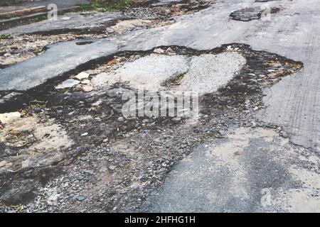 Una strada danneggiata da pioggia e neve, che necessita di manutenzione. Pavimentazione asfaltata rotta con conseguente buche, pericolosa per i veicoli. Foto Stock