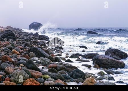 Giorno tempestoso e nuvoloso con pietre rotolanti colorate sulla spiaggia Molen. Geopark globale UNESCO vicino Larvik, Vestfold County, Norvegia Foto Stock