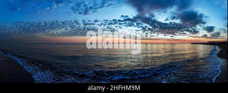 Una panoramica coinvolgente di un sensazionale e imperdibile tramonto sul mare con un fantastico cielo con nuvole di cirrus dipinge il firmamento avvolto in un romantico blu Foto Stock