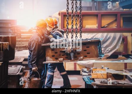 Interni di fabbrica di metallo con operai in caschi e lavoro uniforme con stampo per ghisa. Produzione industriale di metalli. Foto Stock