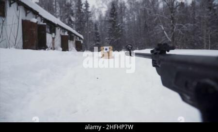 Un uomo che punta una pistola a pellet verso un bersaglio, praticando il suo obiettivo in inverno. Clip. Lo sparatutto in camouflage mira a un bersaglio con un fucile con un'op Foto Stock