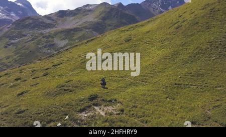 Vista aerea di un uomo a cavallo su una verde montagna pendio. Bella giornata estiva, catena montuosa, cielo nuvoloso e verde erba fresca che copre il hi Foto Stock