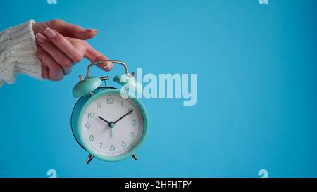 Primo piano della mano della donna che tiene blu retro sveglia sfondo blu, l'ora su orologio è dieci minuti, 10:10.Time per svegliarsi, mattina presto.B. Foto Stock