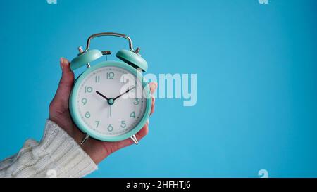 Primo piano della mano della donna che tiene blu retro sveglia sfondo blu, l'ora su orologio è dieci minuti, 10:10.Time per svegliarsi, mattina presto.B. Foto Stock