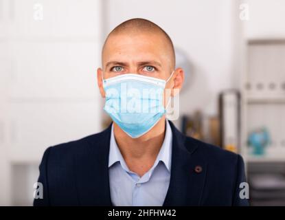 Uomo manager in maschera medica in piedi in ufficio moderno Foto Stock