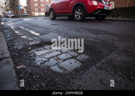 Una grande pothole che espone il lavoro di mattone nella strada Foto Stock