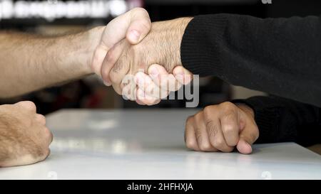 Primo piano di un tavolo e mani di due uomini che hanno intervista o dialogo. Concetto di negoziazione, il successo della gente di affari scuotendo le mani mentre fa agre Foto Stock
