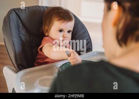 Ragazza del bambino sorridente sudicia che mangia con un cucchiaio in seggiolone. Nutrizione organica naturale. Cibo biologico. Cura del bambino. Foto Stock