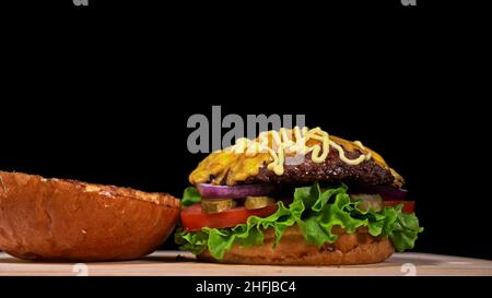 Craft burger di cottura è su sfondo nero. Sono costituiti da: salsa, lattuga, pomodoro, cipolla rossa, sottaceti, formaggi, pancetta, aria bun e in marmo la carne di manzo. Foto Stock