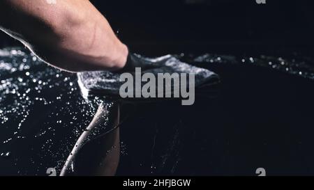 Utilizzando uno straccio nel palmo della tua mano, gocce vengono rimossi dall'auto. Flusso di discesa verso il basso il cofano. Vista ravvicinata del cofano auto. Lucidatura e lavaggio auto. Foto Stock