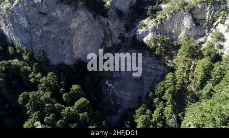 Macchina fotografica che si allontana dal pendio boscoso con rocce in una giornata estiva soleggiata. Antenna di molti alberi di abete verde che crescono su un ripido pendio di montagna, beau Foto Stock