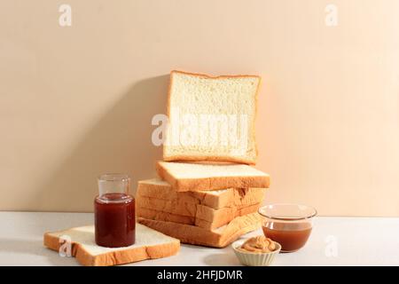 Pane bianco accatastato con burro di arachidi, marmellata di fragole e salsa al caramello, spazio copia per testo Foto Stock