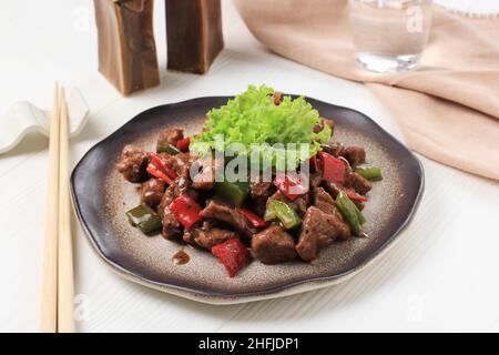 Asian Food: Manzo Teriyaki con peperoni rossi e verdi, primo piano su un piatto su un tavolo bianco. Immagine orizzontale Foto Stock