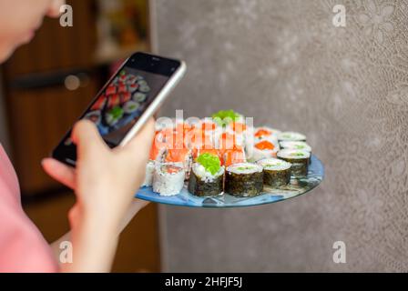 Preparazione di sushi e panini a casa. Sushi con frutti di mare, insalata e riso bianco. Cibo per la famiglia e gli amici. Una ragazza scatta le immagini sul suo telefono di un insieme di Foto Stock