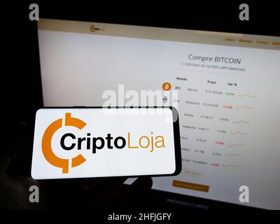 Persona che detiene il cellulare con il logo della società portoghese Smart Token Lda. (CriptoLoja) sullo schermo di fronte alla pagina web. Mettere a fuoco sul display del telefono. Foto Stock