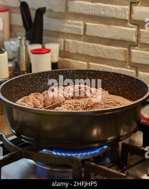 Lo chef frigge i panini di carne in una padella su una stufa a gas. Cucina gourmet francese Foto Stock