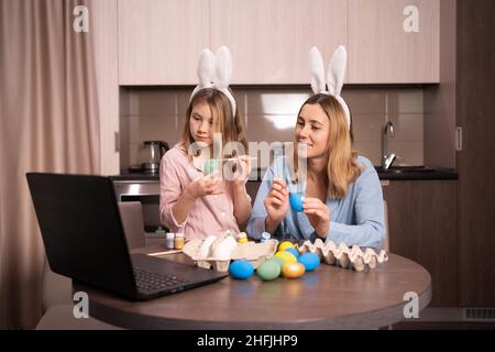 Le ragazze di Pasqua dipingono le uova, registrano le lezioni su una webcam con un portatile. Madre e figlia si preparano per la vacanza insieme. Spazio copia. Foto Stock