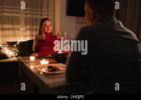 Felice giovane coppia in amore bere vino, godere di conversazioni, festeggiare San Valentino, organizzare cena romantica con candele a casa, seduta Foto Stock