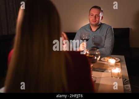 Felice giovane coppia in amore bere vino, data romantica, gli amanti celebrare San Valentino, uomo e donna cena con candele a casa seduta a tavola, Foto Stock