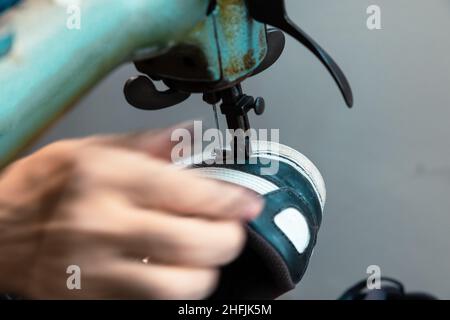 Copriscarpe. Calzolaio che ripara una sneaker sulla macchina da cucire. Sfocatura del movimento sulla mano del calzolaio. Messa a fuoco selettiva. Foto Stock